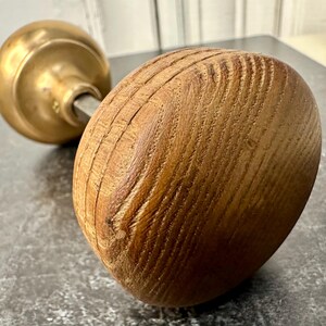 May include: A brass door knob with a wooden handle. The handle is round and has a wood grain pattern. The knob is polished and shiny.