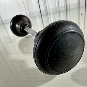 May include: A black door knob with a silver spindle. The knob has a rounded shape and a smooth surface.