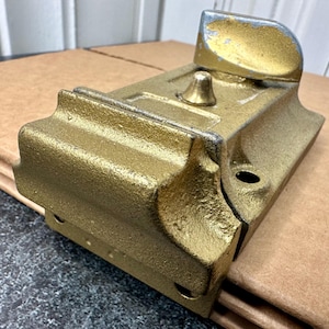 May include: A gold-colored metal door latch with a silver-colored lever handle. The latch has a rounded, decorative design and a keyhole.