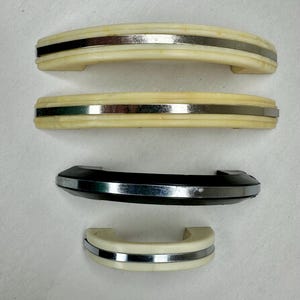 May include: Four cabinet handles in a row. Two are off-white with a silver stripe, one is black with a silver stripe, and the last is off-white with a silver stripe. The handles have a curved design.