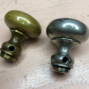 May include: Two antique door knobs, one is brass and the other is silver. Both have a round shape and a hole in the bottom.
