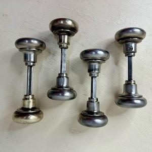 May include: Five antique silver door knobs with a round, domed shape and a long, cylindrical stem. The knobs have a worn, aged finish.