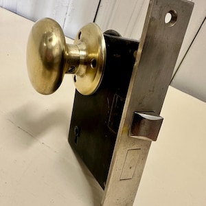 May include: A vintage brass door knob and lock set with a round knob and a rectangular plate. The lock has a keyhole and a latch.