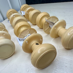 May include: A collection of vintage, cream-colored door knobs. The knobs have a rounded, oval shape and are arranged in rows. Each knob has a circular base with screw holes. Some knobs have price tags attached.