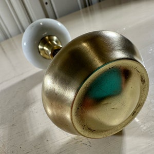May include: A gold door knob with a white porcelain handle. The knob is round and has a smooth, polished finish.