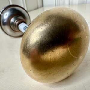 May include: A gold-colored, egg-shaped object with a metallic, silver-colored base. The object has a smooth, reflective surface with visible scratches. The base is cylindrical and attached to the egg-shaped top.
