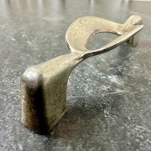 May include: A silver-toned, abstract metal sculpture with a curved, flowing design. The sculpture features a rectangular base and a loop-like shape with an open center. The metal has a textured, aged appearance, suggesting it may be vintage or antique.