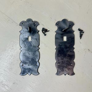 May include: Two decorative, dark metal door latches with ornate edges and a keyhole. Each latch has a curved top and bottom with a hook and comes with several small screws. The latches have a distressed, aged appearance.