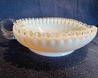 May include: A white milk glass bowl with a silver rim and a clear glass handle. The bowl has a scalloped edge and a footed base.