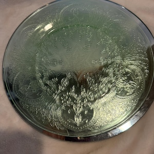 May include: A green glass serving plate with a silver rim and an embossed floral design.