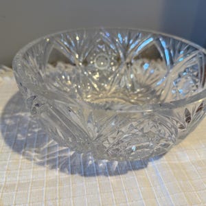 May include: A clear, cut-glass bowl with a detailed starburst pattern. The bowl is round with a wide opening and sits on a white surface. The intricate design catches the light, creating a sparkling effect. A decorative piece for serving or display.