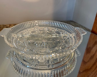 May include: A clear glass serving dish with a divided center section and two handles. The dish has a decorative, cut-glass pattern.