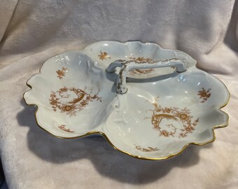 May include: A white porcelain serving dish with three sections and a gold handle. The dish is decorated with a brown floral pattern.
