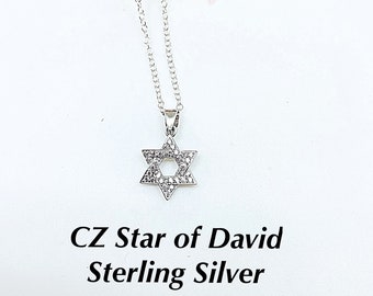 May include: A silver chain necklace with a star of David pendant encrusted with clear cubic zirconia stones. The pendant is surrounded by pink roses. The text "CZ Star of David Sterling Silver" is written below the pendant.