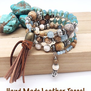 May include: A multi-strand bracelet with brown, white, and blue beads, accented with silver and gold accents. The bracelet has a brown leather tassel.