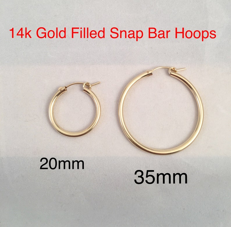 May include: Two pairs of 14k gold filled snap bar hoop earrings. The smaller pair is 20mm in diameter and the larger pair is 35mm in diameter.