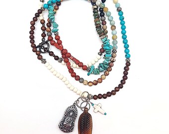 Puede incluir: Collar multicadena con cuentas marrones, blancas, rojas, azules y turquesas. El collar tiene un dije de plata con una figura de Buda, un dije de plata en forma de cruz y un dije de pluma marrón.