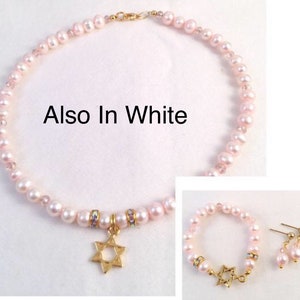 May include: A pink pearl necklace with a gold Star of David pendant. The necklace is also available in white. The image also shows a matching bracelet and earrings.