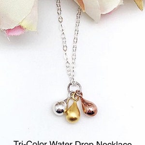 Puede incluir: Un collar de cadena de plata con un colgante que presenta tres abalorios en forma de lágrima en plata, oro y oro rosa.