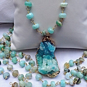 May include: A long, layered necklace with a large, aqua blue and green crystal pendant. The necklace is made of gold chain and small, faceted aqua blue beads.