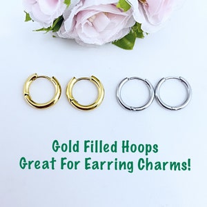 Puede incluir: Dos pares de aros, un par es de oro lleno y el otro es de plata. Los pendientes están sobre un fondo blanco con flores rosas. El texto "Gold Filled Hoops Great For Earring Charms!" está debajo de los pendientes.