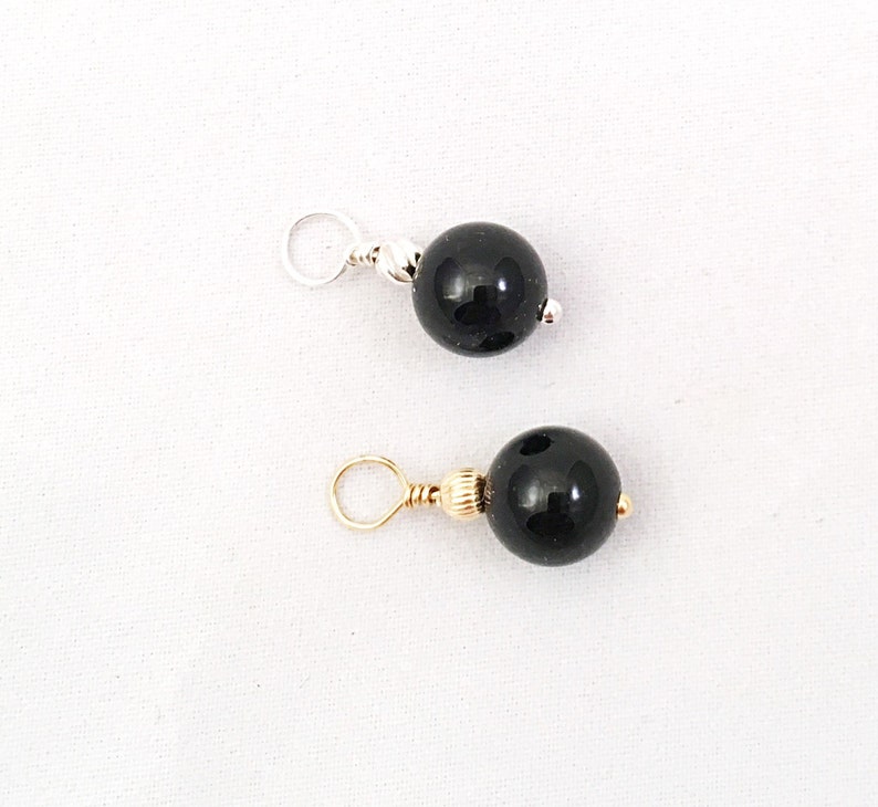 May include: Two black bead charms with gold and silver jump rings. The beads are round and smooth.