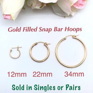 May include: Three gold-filled snap bar hoops in different sizes: 12mm, 22mm, and 34mm. The hoops are on a white background. "Gold Filled Snap Bar Hoops" and "Sold in Singles or Pairs" are written below the hoops.