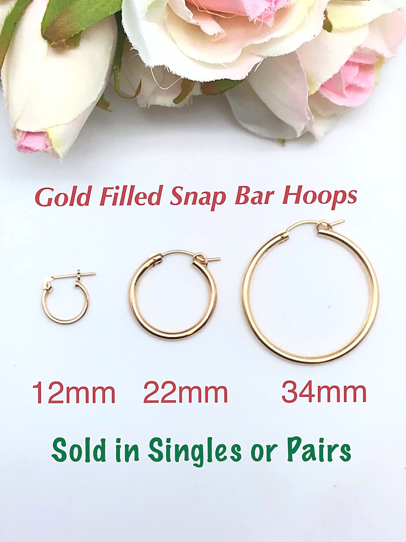 May include: Three gold-filled snap bar hoops in different sizes: 12mm, 22mm, and 34mm. The hoops are on a white background. "Gold Filled Snap Bar Hoops" and "Sold in Singles or Pairs" are written below the hoops.