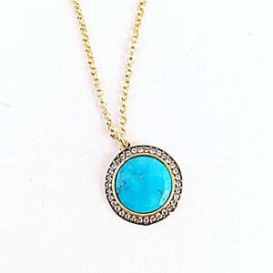 May include: A gold chain necklace with a turquoise stone pendant surrounded by a halo of clear stones.