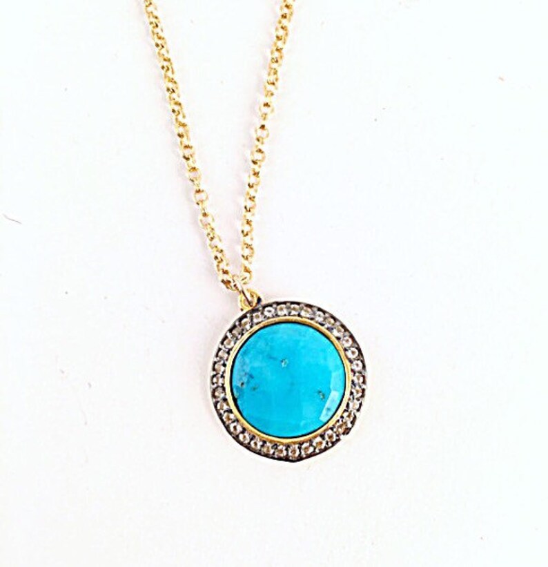 May include: A gold chain necklace with a turquoise stone pendant surrounded by a halo of clear stones.