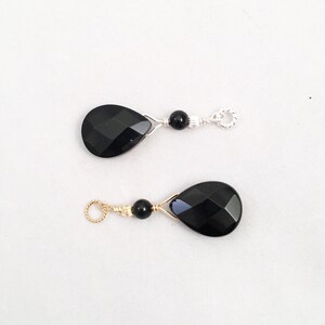May include: Two black gemstone teardrop pendants with gold wire wrapped around them. Each pendant has a small black bead and a gold or silver jump ring.