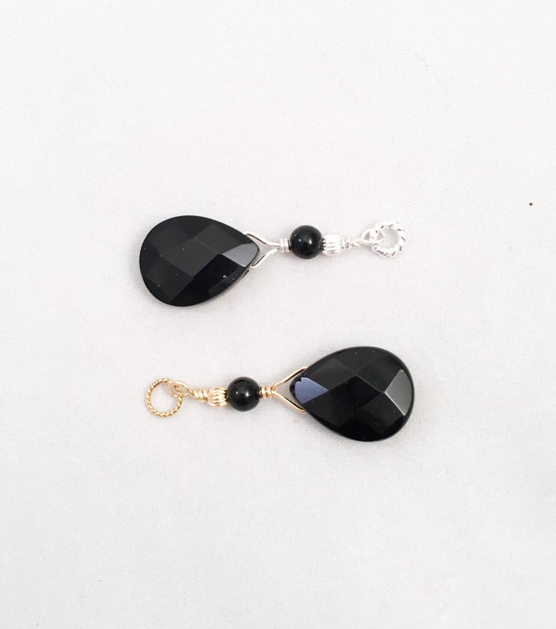 May include: Two black gemstone teardrop pendants with gold wire wrapped around them. Each pendant has a small black bead and a gold or silver jump ring.