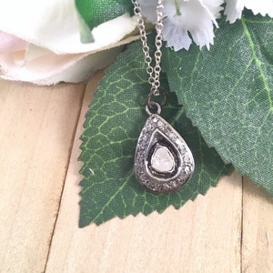 Puede incluir: Un collar de plata con un colgante en forma de l&aacute;grima, adornado con un gran diamante en bruto en el centro. El diamante est&aacute; rodeado de diamantes m&aacute;s peque&ntilde;os engastados en plata.