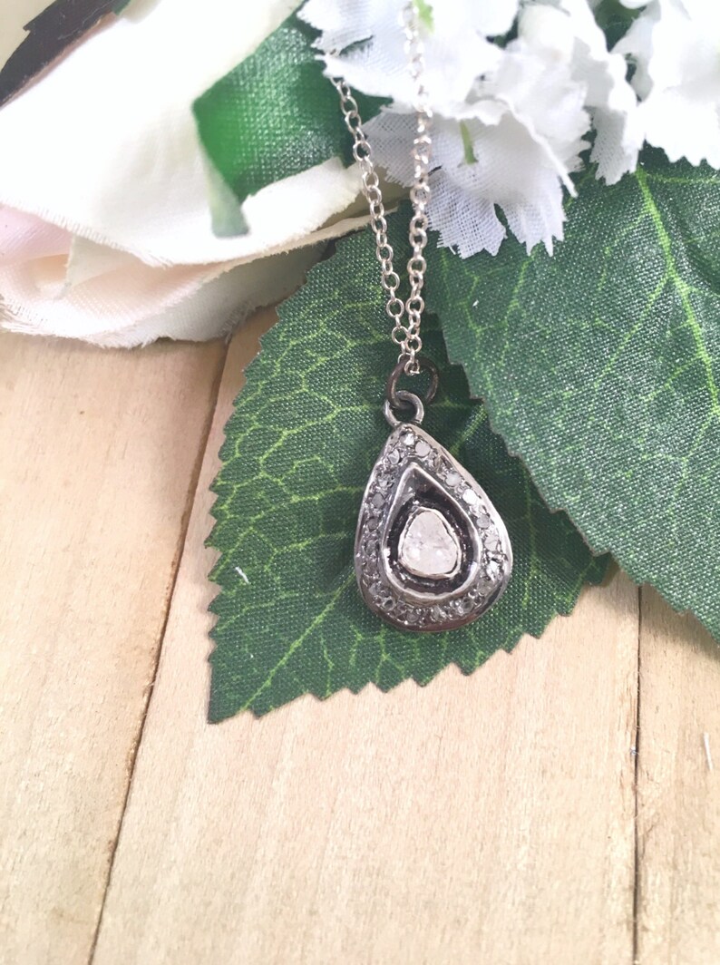 Puede incluir: Un collar de plata con un colgante en forma de l&aacute;grima, adornado con un gran diamante en bruto en el centro. El diamante est&aacute; rodeado de diamantes m&aacute;s peque&ntilde;os engastados en plata.