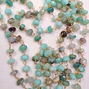 May include: A long necklace made of light blue and green gemstone beads strung on a gold chain. The beads are faceted and have a natural, organic look.