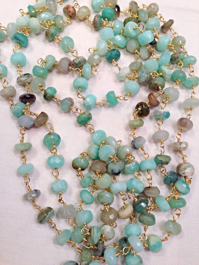 May include: A long necklace made of light blue and green gemstone beads strung on a gold chain. The beads are faceted and have a natural, organic look.