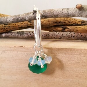 May include: Silver hoop earrings with a green gemstone and white beads dangling from the bottom.