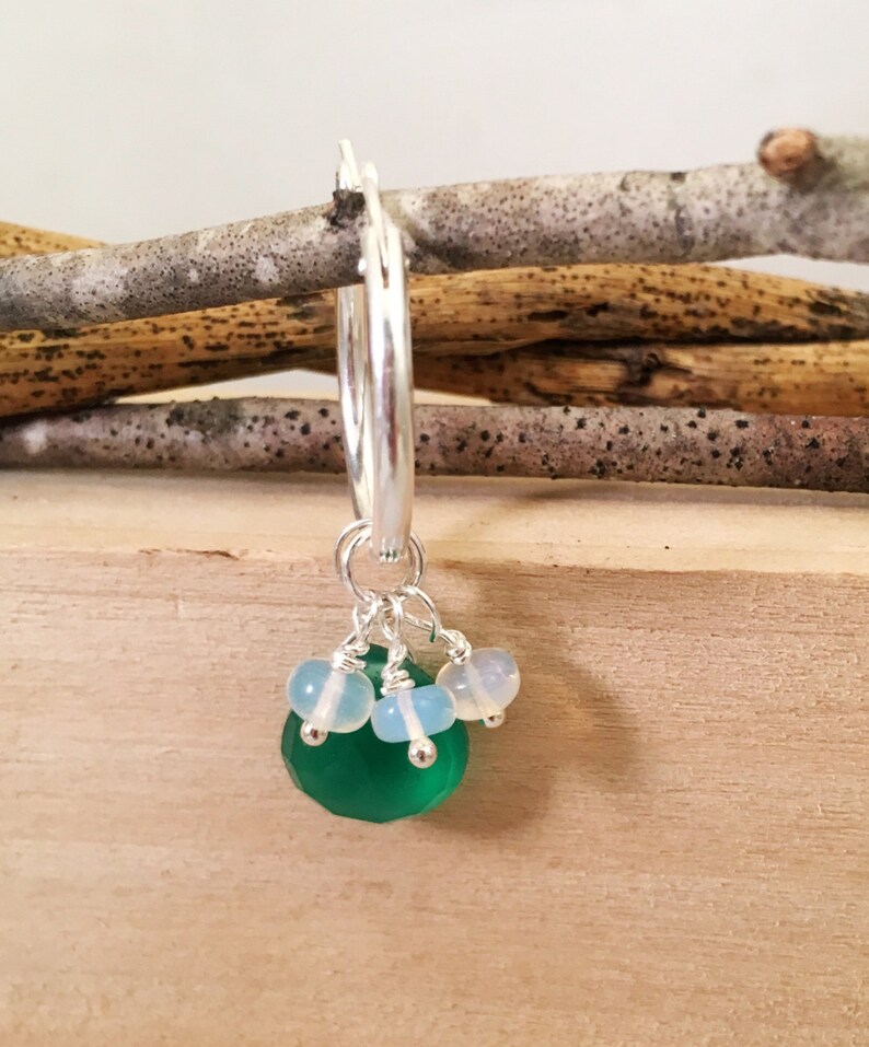 May include: Silver hoop earrings with a green gemstone and white beads dangling from the bottom.