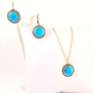May include: A gold necklace and earrings set with turquoise stones surrounded by a halo of smaller stones. The pendant and earrings are round.
