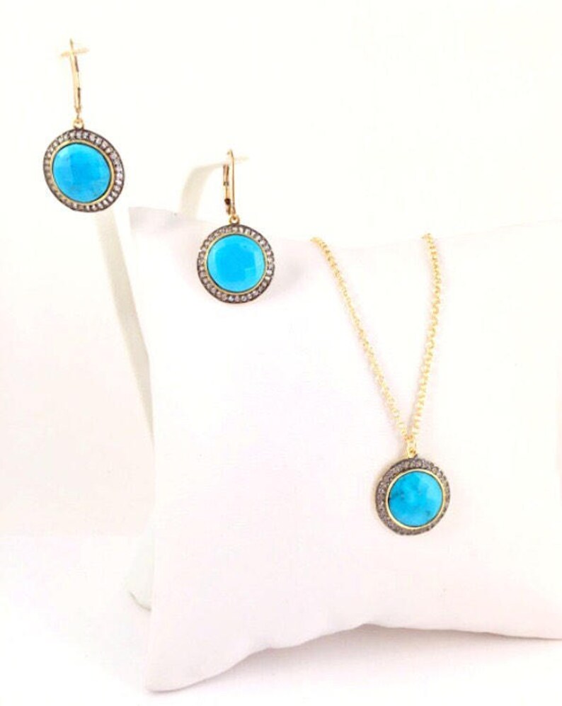 May include: A gold necklace and earrings set with turquoise stones surrounded by a halo of smaller stones. The pendant and earrings are round.