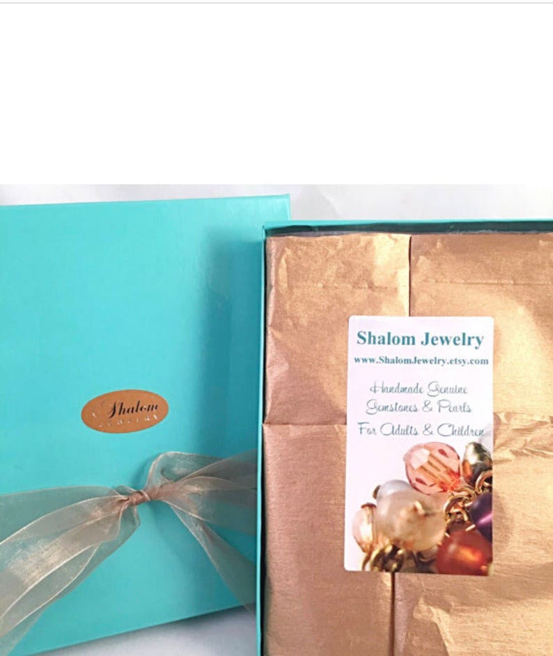 May include: A turquoise gift box with a gold ribbon and a label that says "Shalom Jewelry" is open to reveal brown tissue paper. The tissue paper has a label that says "Shalom Jewelry www.ShalomJewelry.etsy.com Handmade Genuine Gemstones & Pearls For Adults & Children".