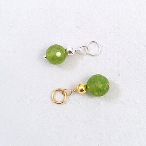 May include: Two green gemstone beads with silver and gold jump rings. The beads are faceted and have a light green color.