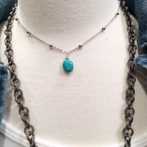 May include: A silver chain necklace with small silver beads and a turquoise pendant. The necklace is on a white mannequin.