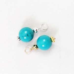 May include: Two turquoise gemstone beads with silver and gold accents. The beads are attached to silver and gold jump rings.
