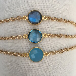 May include: Three gold chain bracelets with different blue gemstone charms. The charms are round and have a faceted design.