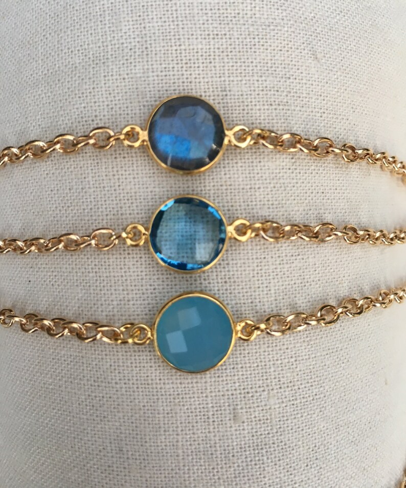 May include: Three gold chain bracelets with different blue gemstone charms. The charms are round and have a faceted design.