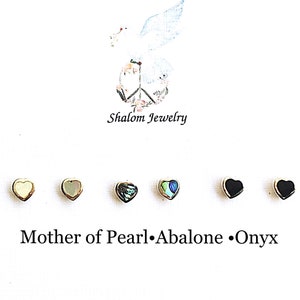 May include: Six heart-shaped earrings in different colors. The earrings are made of mother of pearl, abalone, and onyx. The text "Mother of Pearl, Abalone, Onyx" is written below the earrings. The text "Shalom Jewelry" is written above the earrings.