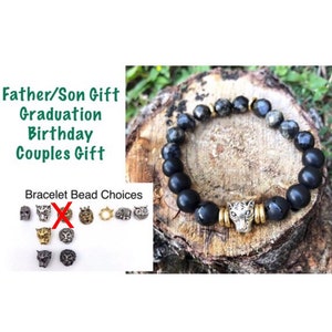 May include: Black beaded bracelet with a gold animal head charm. The bracelet is on a wooden surface. The image also shows a variety of other animal head charms to choose from.