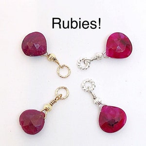 May include: Four ruby gemstone pendants with gold and silver chain links. The rubies are heart-shaped and have a deep red color. The word "Rubies!" is written in white text above the pendants.