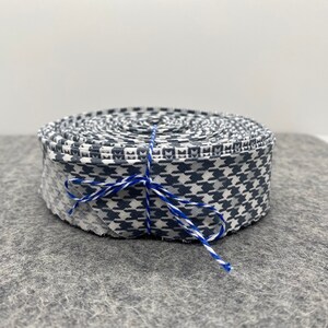 May include: A roll of white and blue patterned fabric ribbon tied with blue and white twine. The ribbon is rolled up and tied with twine.